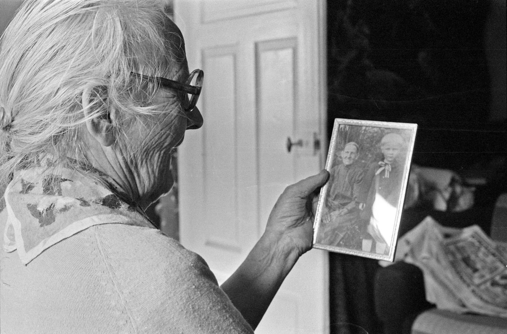 Vanha nainen pitelee kädessäänmustavalkoista valokuvaa naisesta ja lapsesta.