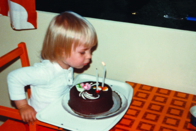 Tyttö puhaltaa 2-vuotissyntymäpäiväkakun kynttilöitä.